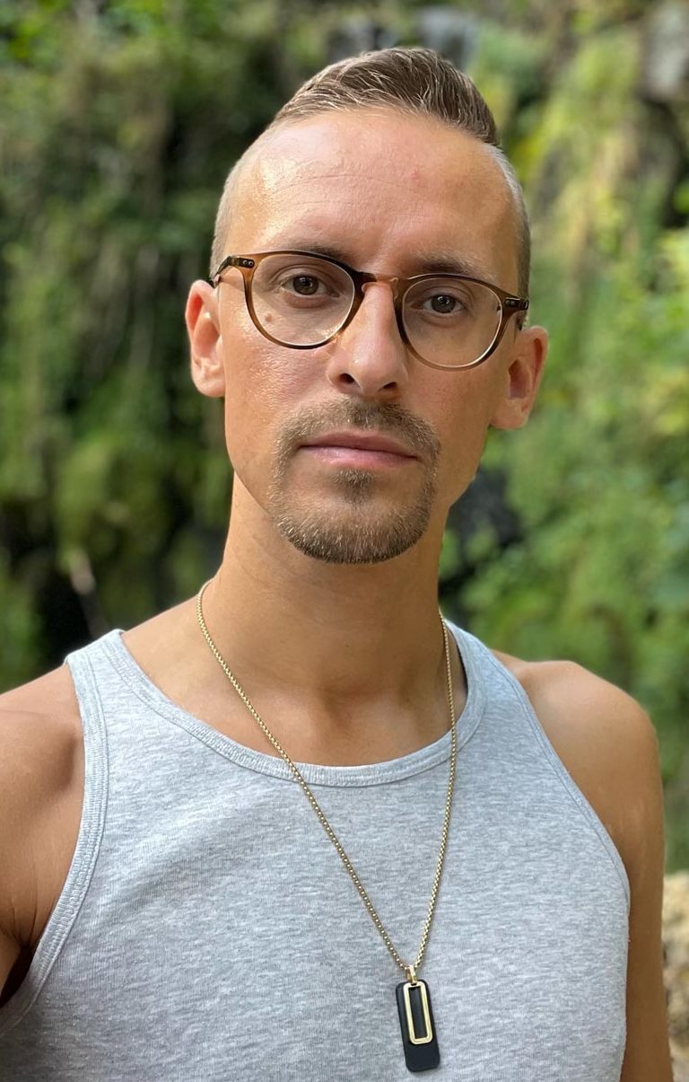 Mann mit Brille und kurzem Haar, trägt ein graues Tanktop, Hintergrund mit Natur. Christopher Keilich Inhaber der Praxis HOLERYA